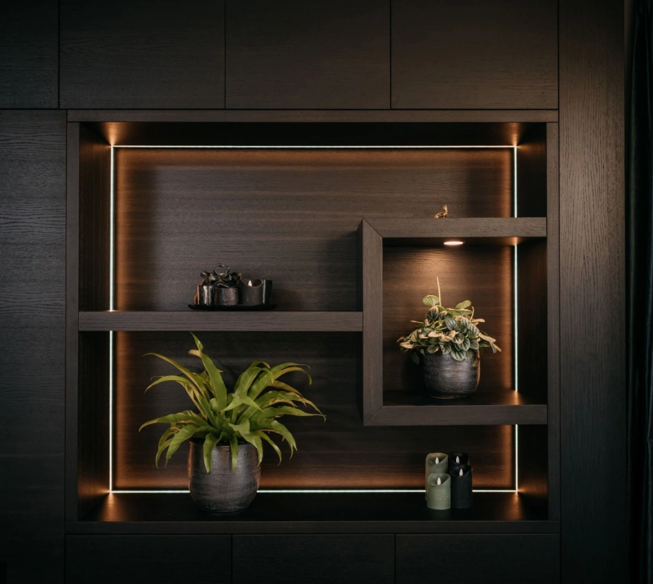 Een moderne houten wandplank met ingebouwde LED-verlichting toont groene planten in potten en kleine decoratieve voorwerpen en creëert zo een stijlvolle en minimalistische look.