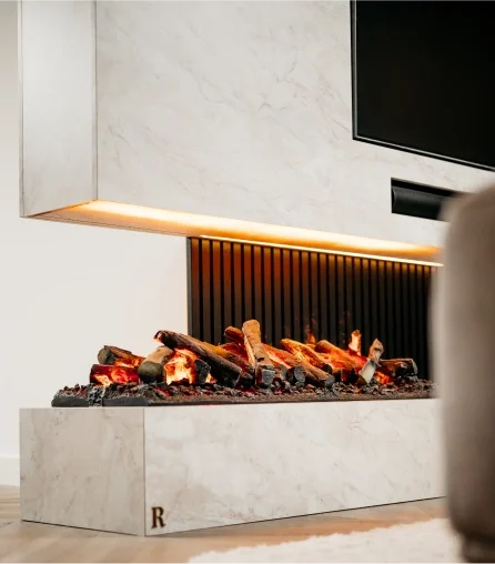 Een moderne elektrische haard met realistisch ogende houtblokken en gloeiende sintels, in een slanke wit marmeren ombouw met een zwarte gegroefde achterwand en warme LED-verlichting onder de schouw.