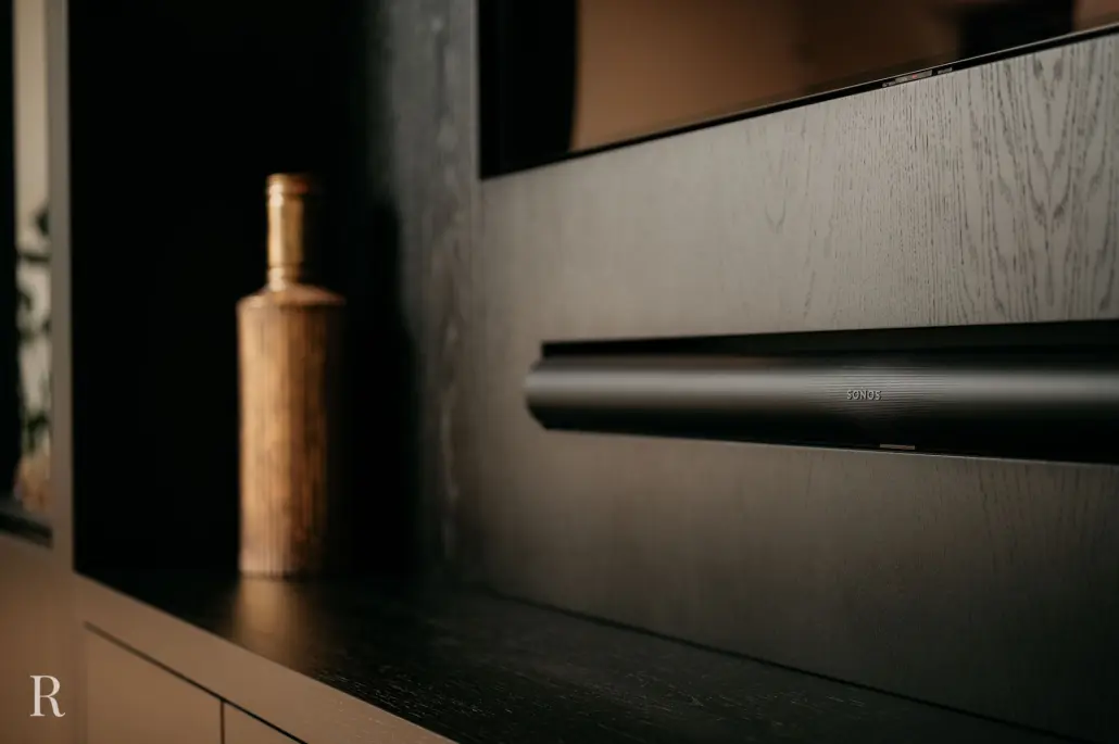 Een close-up van een moderne zwarte tv-standaard met een decoratieve houten fles en een strakke zwarte soundbar onder een aan de muur gemonteerde flatscreen-tv.