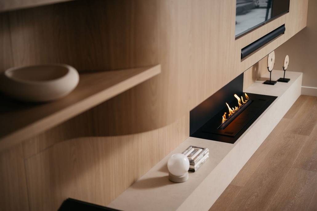 Een moderne leefruimte met een ingebouwde lineaire gashaard onder een gemonteerde tv, met licht houten lambrisering, minimalistische planken, decoratieve voorwerpen en lichte hardhouten vloeren.