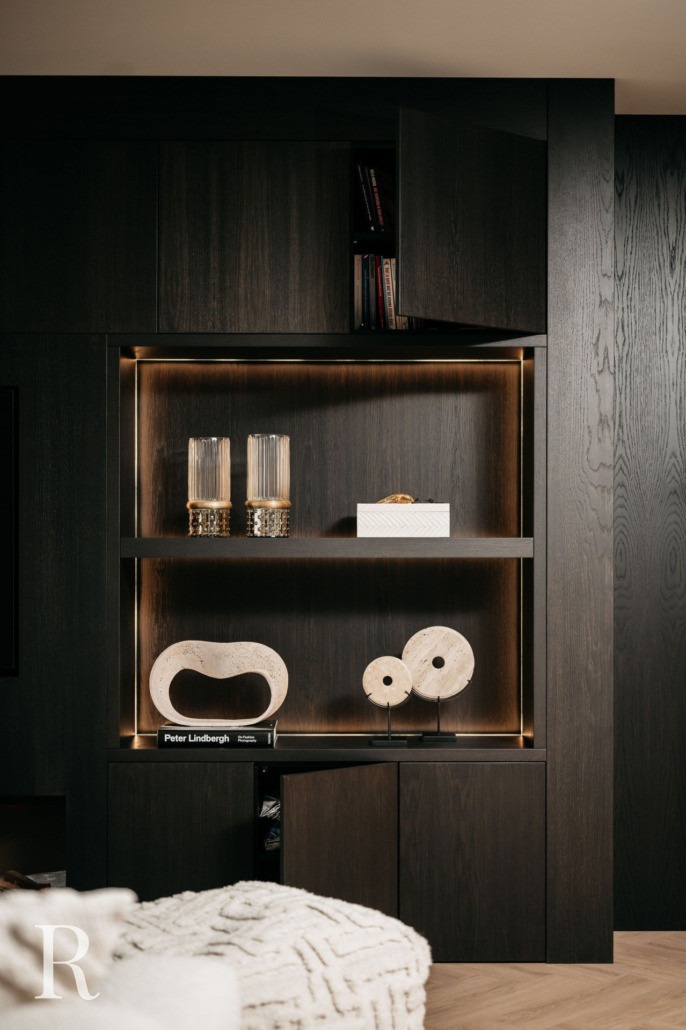 Een moderne donkerhouten kast met ingebouwde verlichting toont decoratieve voorwerpen, waaronder twee glazen vazen, een witte doos, abstracte stenen beelden en boeken. Sommige kastdeuren zijn iets open.