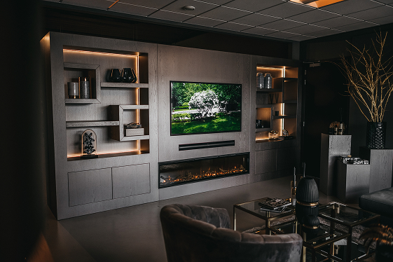 Een moderne woonkamer met ingebouwde planken, een tv aan de muur met een tuintafereel, een lineaire elektrische open haard eronder en eigentijds meubilair, alles in donkere, stijlvolle tinten en zachte sfeerverlichting.