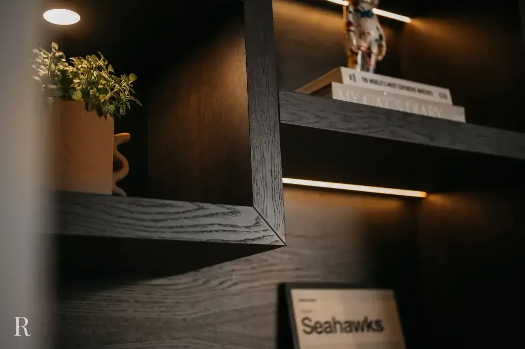 Een close-up van donkere houten planken met warme verlichting, met daarop een potplant, een stapel boeken, een klein beeldje en een ingelijste krant met een zichtbare kop over de Seahawks.