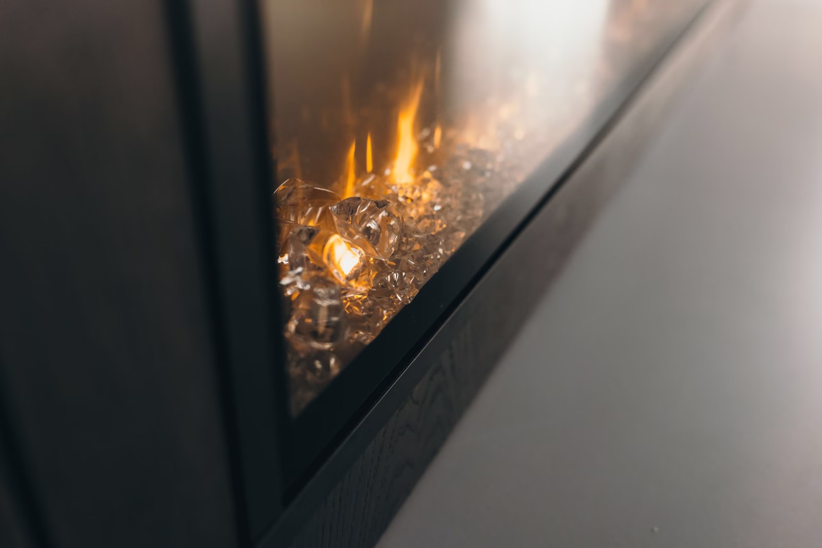Close-up van een moderne elektrische open haard met decoratieve glaskristallen en realistische geeloranje vlammen achter een glazen paneel, in een strak donker frame.