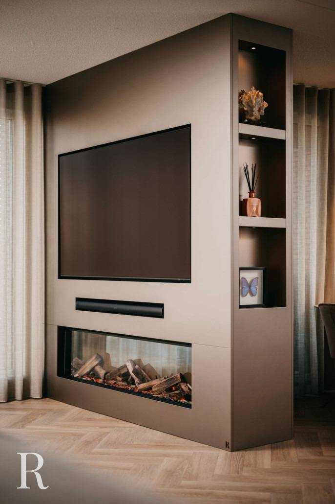 Een moderne woonkamer heeft een grote tv aan de muur boven een ingebouwde elektrische open haard. Planken aan de zijkant tonen decoratieve voorwerpen, waaronder een diffuser, een schelp en een vlinderframe. Een lichte houten vloer en transparante gordijnen maken de ruimte compleet.