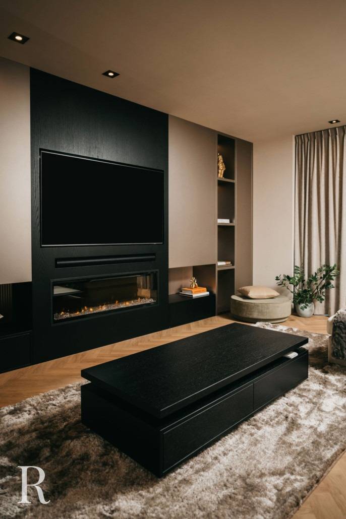 Moderne woonkamer met een tv aan de muur boven een strakke elektrische open haard, ingebouwde planken, een zwarte salontafel, pluche vloerkleed, beige gordijnen en een ronde poef naast een bladplant. Warm, neutraal kleurenpalet.