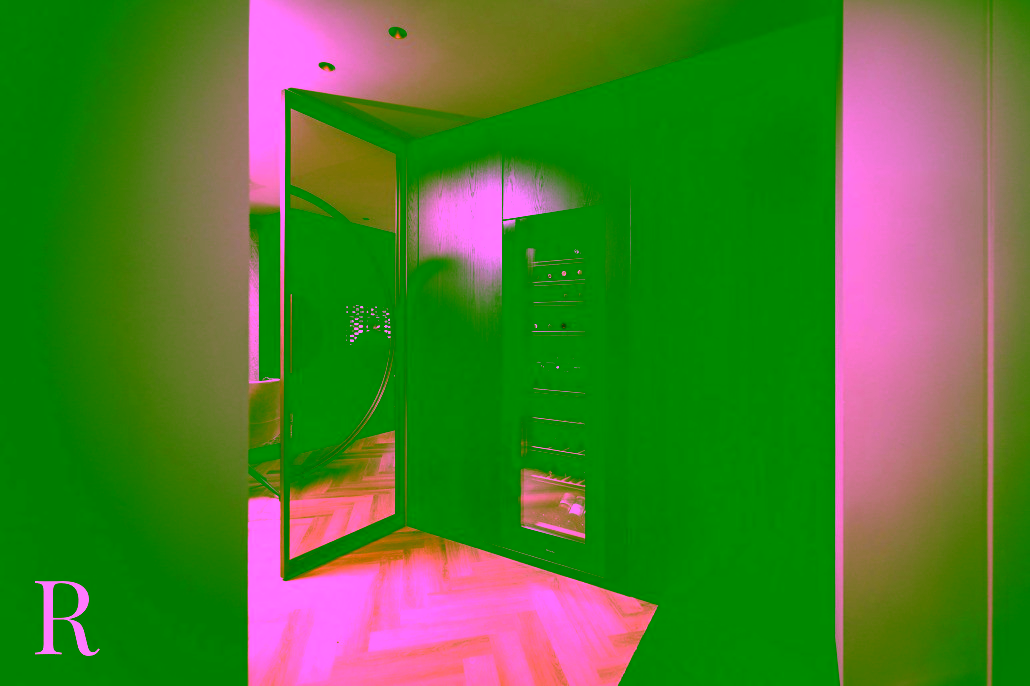 Een moderne wijnkelder met een glazen wijnkoelkast ingebouwd in een donkerhouten muur, een grote ronde spiegeldeur en lichte visgraat houten vloeren. De ruimte is zacht verlicht, wat een luxe gevoel geeft.