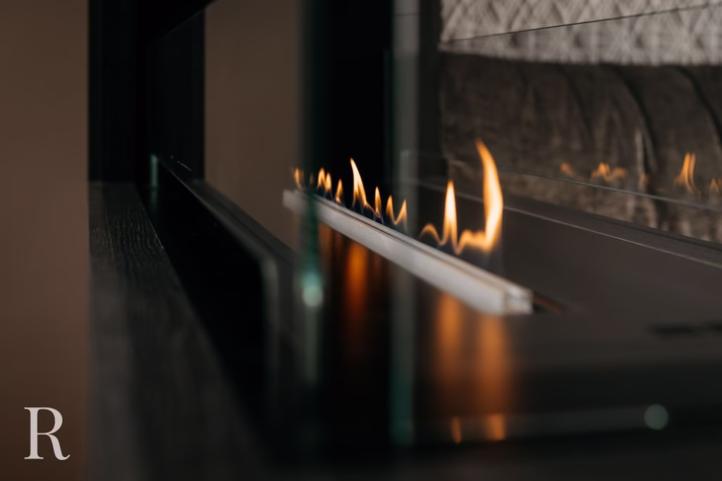 Een close-up van een moderne lineaire open haard met kleine, heldere vlammen achter heldere glazen panelen. De omgeving ziet er elegant en eigentijds uit, met een muur met textuur zichtbaar op de achtergrond.