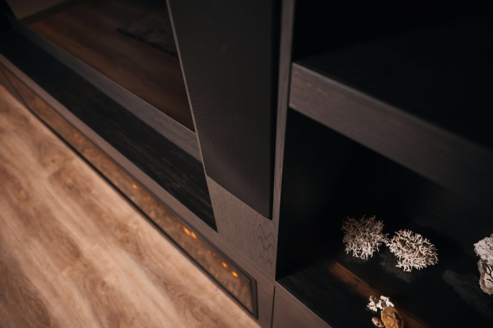 Een close-up van een donkere houten plank met decoratieve witte koraalstukken op een lagere plank, tegen een lichte houten vloer.