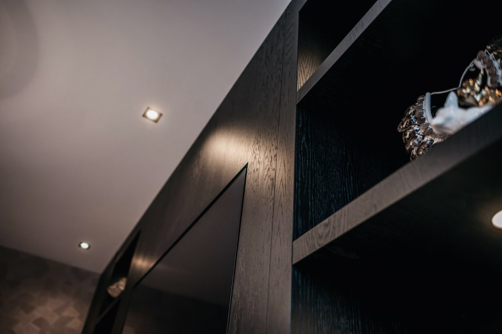 Een close-up, schuine weergave van donkere houten planken en een muur met verzonken plafondverlichting, die een moderne interieursfeer creëren.