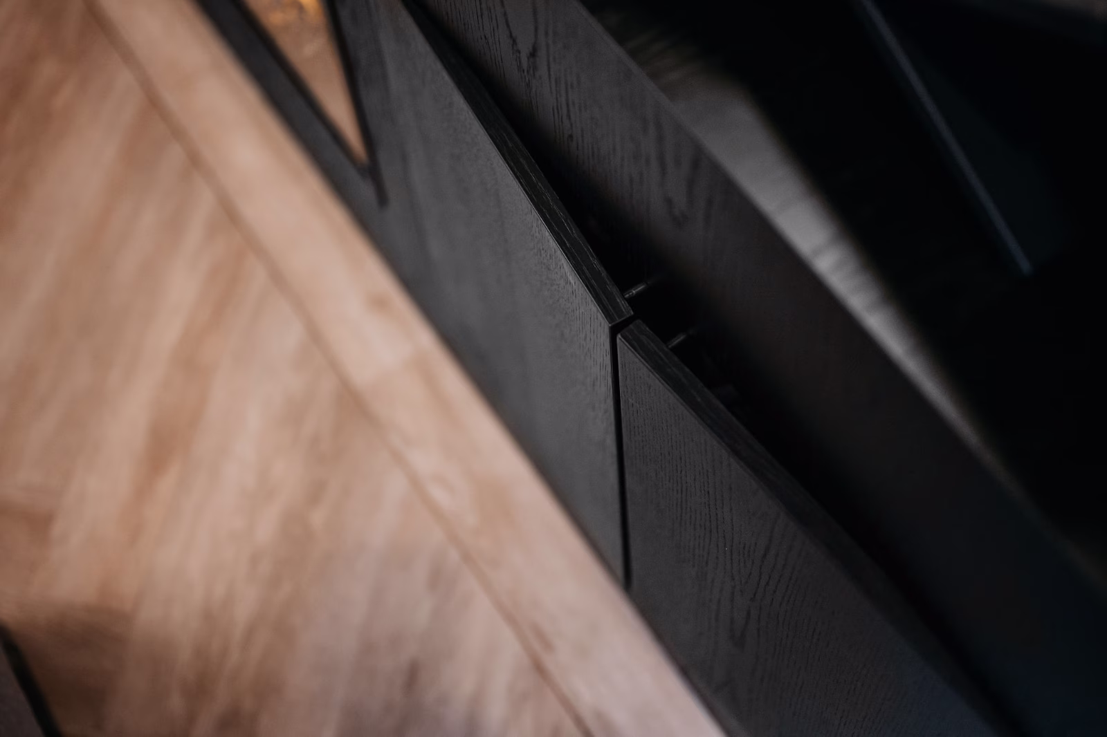 Close-up van een gedeeltelijk geopende donkere houten kastdeur met een lichtgekleurde houten vloer ernaast.