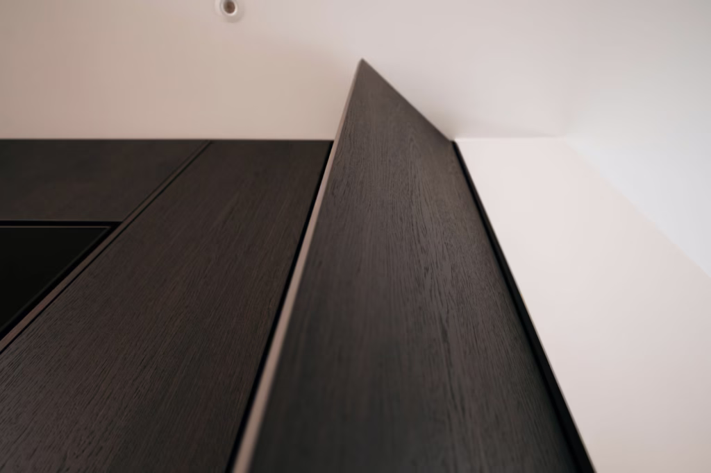 Close-up, opwaartse hoek van een moderne, donkerhouten kastdeur gedeeltelijk open tegen een wit plafond, met nadruk op strakke lijnen en minimalistisch ontwerp.