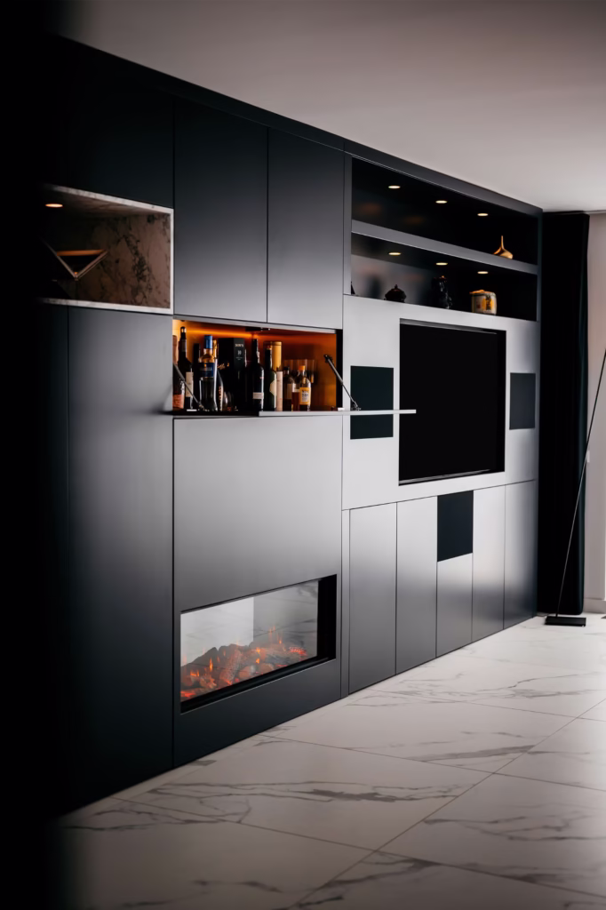 Een modern zwart wandmeubel met ingebouwde planken, een tv, een glazen display met flessen en een elektrische open haard eronder, tegen een marmeren tegelvloer in een hedendaagse woonkamer.