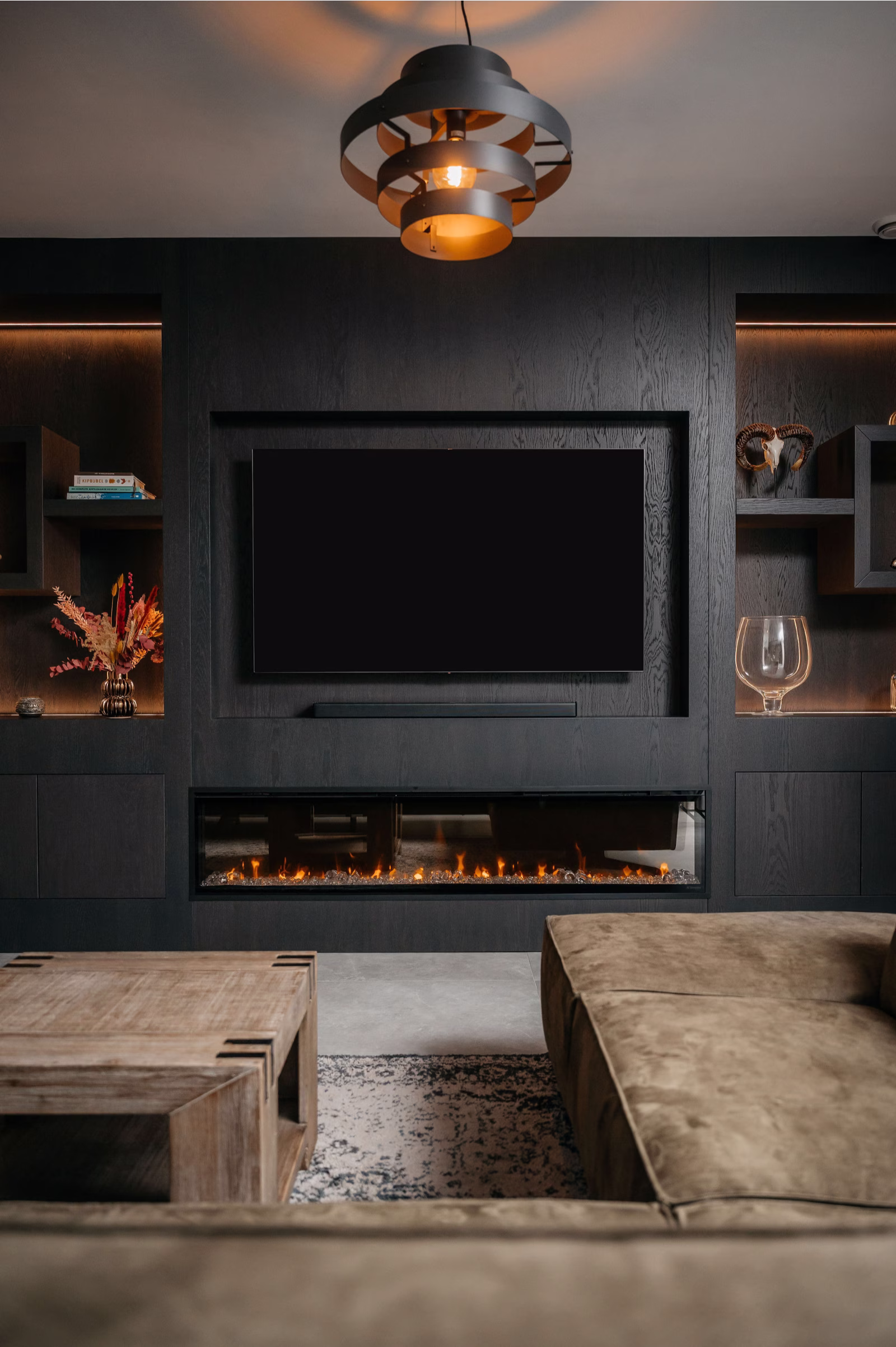 Moderne woonkamer met een zwarte entertainmentmuur, gemonteerde tv, elektrische open haard, planken met decor, een houten salontafel, beige sofa en een eigentijdse plafondlamp.
