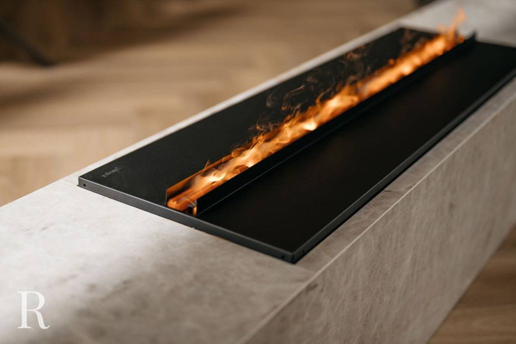 Een moderne rechthoekige haard met een strak zwart frame en zichtbare oranje vlammen, geplaatst in een lichtgekleurd stenen of marmeren oppervlak op een vloer met houtpatroon, vormt een perfecte aanvulling op elke donkerhouten cinewall.