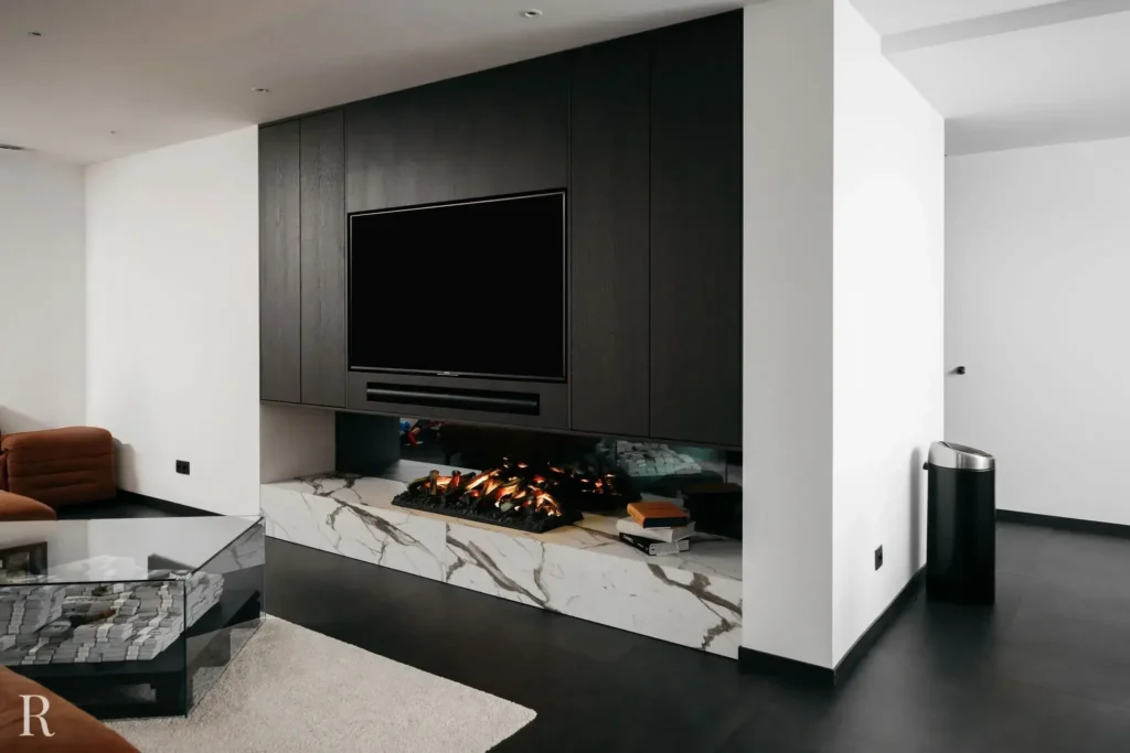 Een moderne woonkamer met een ingebouwde elektrische open haard met marmeren voet, een tv aan de muur, donkerhouten lambrisering, een glazen salontafel en een minimalistische inrichting in neutrale tinten.