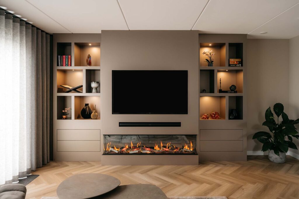 Moderne Japandi-woonkamer met een filmmuur waarop een aan de muur bevestigde tv hangt boven een strakke elektrische haard, ingebouwde planken voor decoratie, lades eronder, een lichte houten visgraatvloer en een grote potplant aan de rechterkant.