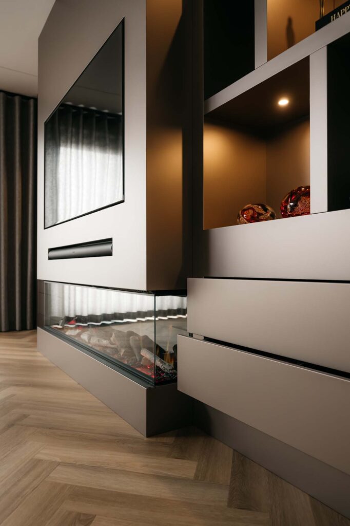 Een moderne Japandi-woonkamer met een filmmuur waarop een aan de muur bevestigde flatscreen-tv hangt, daaronder een open haard met glazen front, open rekken met decoratieve voorwerpen en lades. Een lichte houten visgraatvloer maakt deze rustige ruimte compleet.