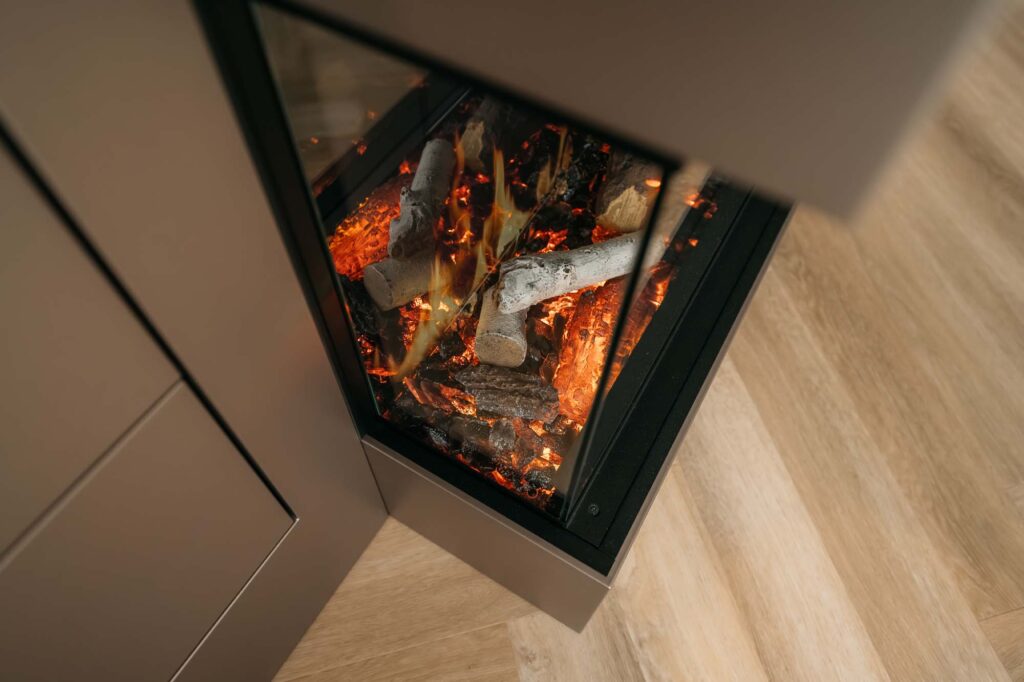 Een close-up van een moderne Japandi-hoekhaard in cinewall-stijl met brandende houtblokken en gloeiende sintels, omgeven door een lichte houten vloer en een metalen omlijsting.